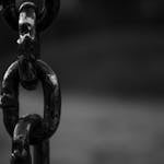 Detailed black and white image of a rusty chain link with blurred background.